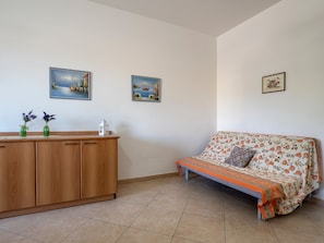 A room with a wooden cabinet, two framed paintings, a floral sofa, and a tiled floor.
