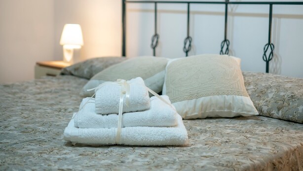 Una cama bien hecha con una colcha de motivos florales, un cabecero metálico y una lámpara de noche.