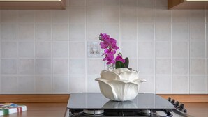 Una cocina con estufa blanca, una olla blanca y una orquídea púrpura sobre la encimera.