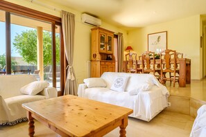 Un salon avec une table en bois, un canapé blanc, un meuble en bois et un coin repas comprenant des chaises et une table.