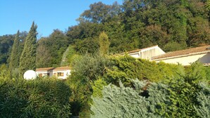 Una vila a la vella, amb teulada de rajola tradicional, envoltada de vegetació abundant i arbres.