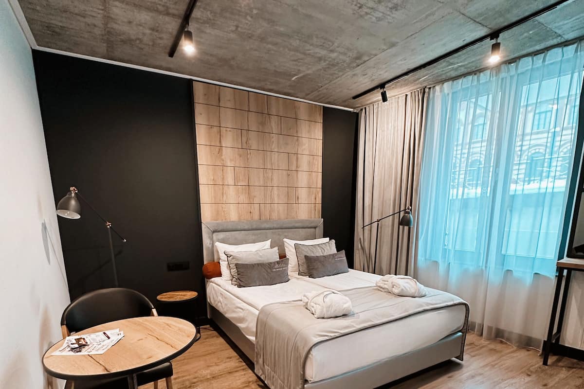 A modern bedroom with a wooden floor, a bed with white bedding, a small round table, and a chair.