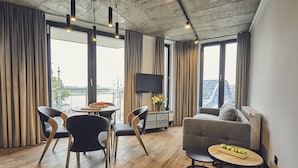Un soggiorno moderno con pavimento in legno, un divano grigio, un tavolo da pranzo con sedie e un televisore su un mobile.
