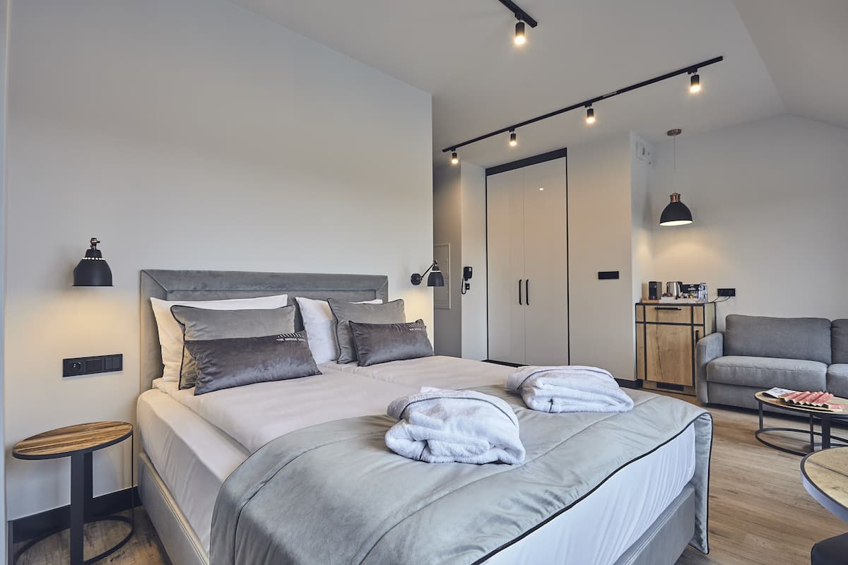 A modern hotel room with a large bed, bedside tables, a desk, and a sofa.