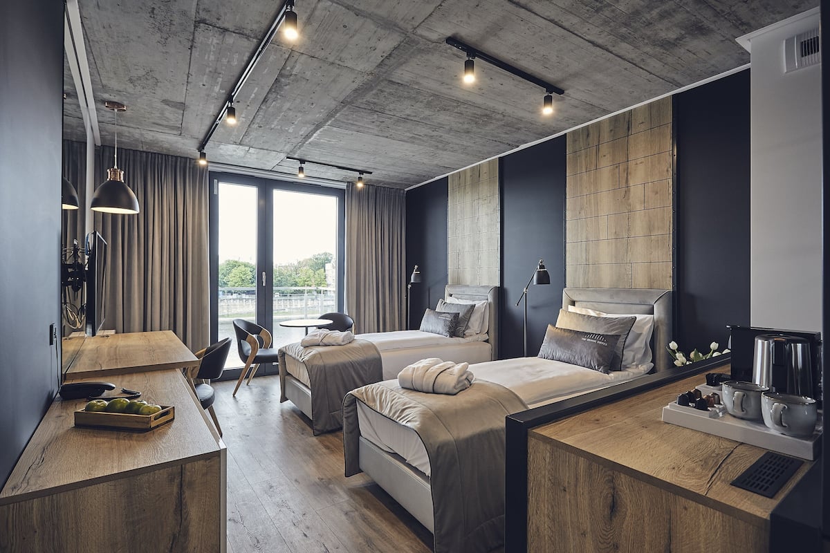 A modern hotel room with two beds, a wooden desk, and a large window.