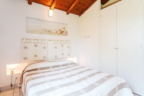 A bedroom with a bed, a nightstand, a wall-mounted light, a ceiling fan, and a door.