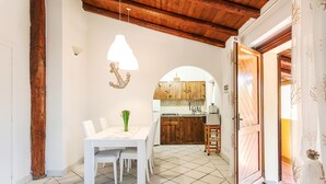 Un comedor con una mesa y sillas blancas, una lámpara colgante y una cocina al fondo.