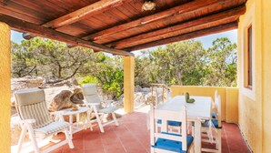Un patio al aire libre con muebles de madera y una mesa, rodeado por un muro amarillo y paisajes naturales.