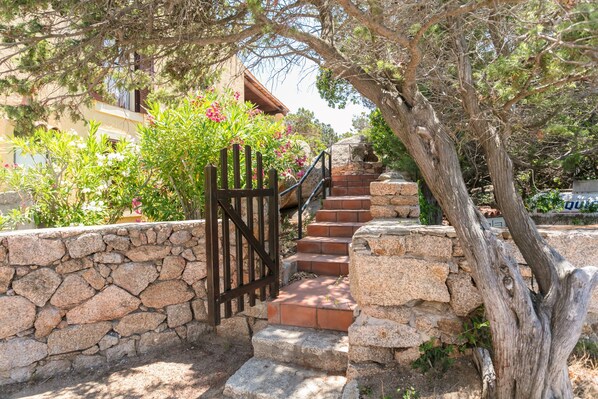 A stone staircase leading to a building with a wooden gate, surrounded by greenery and trees.