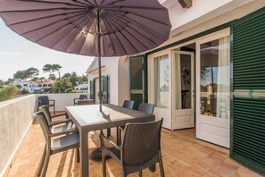 Een balkon met een tafel, stoelen en een parasol, met uitzicht op de omgeving.