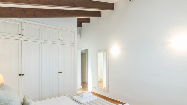 Een slaapkamer met een grote garderobe, een bed met kussens, een nachtkastje en een spiegel.