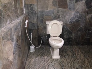 A bathroom with a marble floor and stone walls, featuring a white toilet with a closed lid. - Hamadhi Guest (Hildummulla)