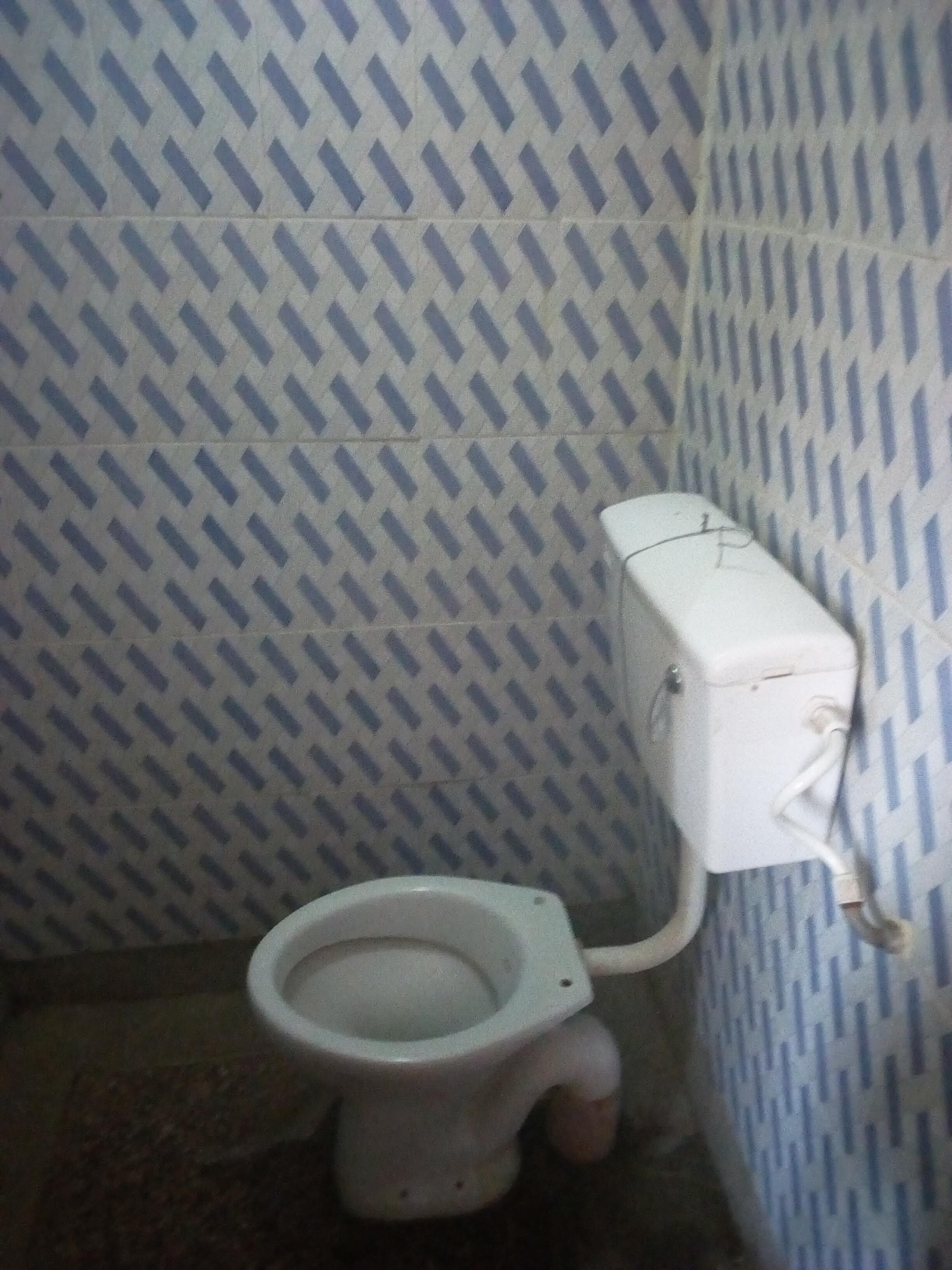 Een kleine, eenvoudige badkamer met een behangwand, een wit toilet en een zichtbare wateraansluiting.