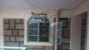 A reception area with a sign above a window, emergency numbers, and a brick wall.