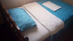 A single bed with a blue and white bedspread, a white pillow, and a wooden headboard.