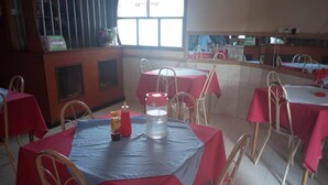 A restaurant interior with tables covered in red tablecloths, white chairs, and a large window allowing natural light.