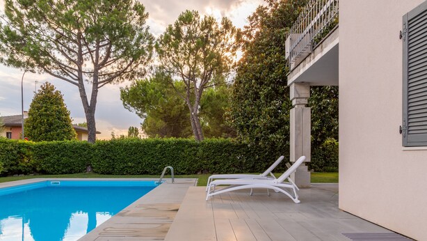 Piscina com espreguiçadeiras, um sebedeiro e um edifício com varanda.