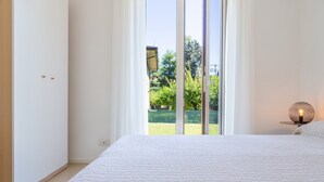 Quarto com uma cama grande, janela com vista para vegetação e mesa de cabeceira com abajur.