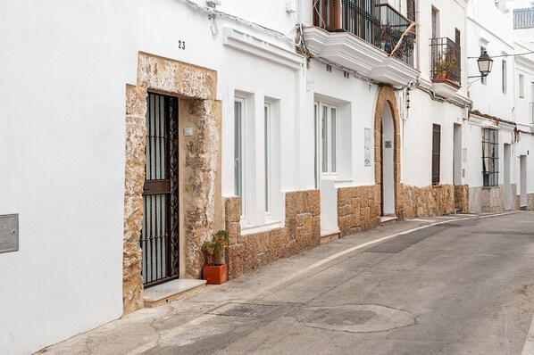 A narrow street lined with white buildings, each with a stone base and a balcony.