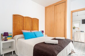 A bedroom with a bed, nightstands, a wooden wardrobe, a television, and a small table with a plant.