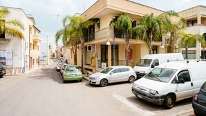 A street with parked cars and a building with balconies and palm trees. - Historical charm in Racale (Racale)