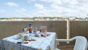 Uma mesa posta em uma varanda, com vista para edifícios ao longe.