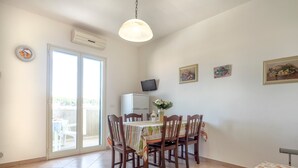 Uma sala de jantar com mesa, cadeiras, televisão e uma porta de vidro deslizante para área externa.