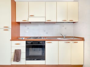 A kitchen with white cabinets, a wooden countertop, a stove, a sink, and an oven.