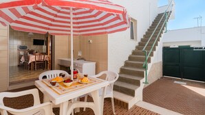 Eine Terrasse mit Tisch, Stühlen und einem gestreiften Sonnenschirm.
