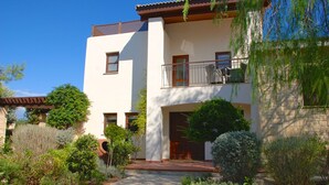 A modern two-story building with a balcony, surrounded by well-maintained gardens and a clear blue sky. - Villa 32 - Limni (Kouklia)
