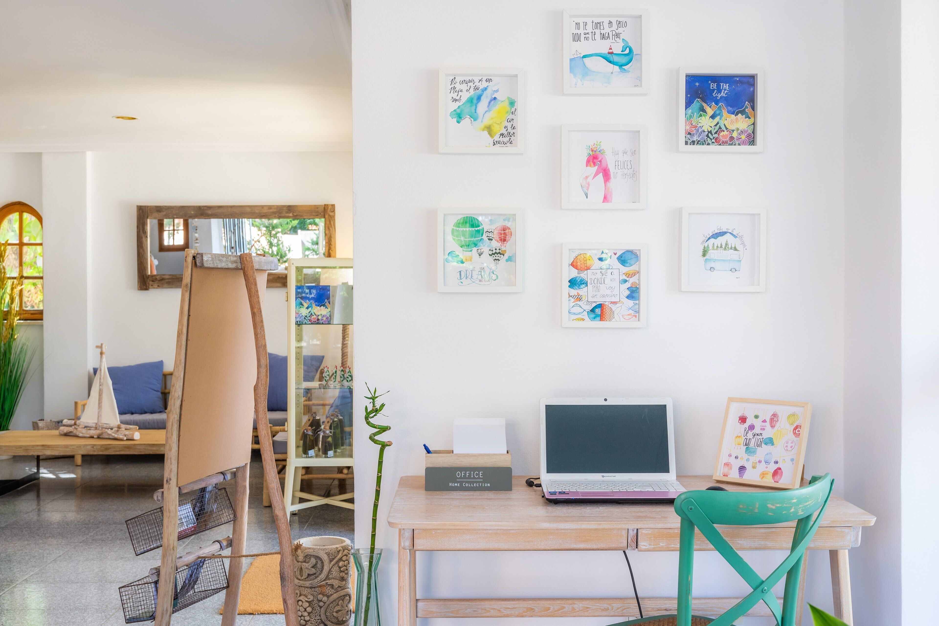 A workspace with a laptop, a desk, a chair, and a collection of framed artworks on the wall.