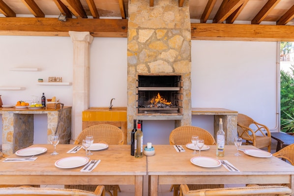 Un área de comedor al aire libre con paredes de piedra, vigas de madera y sillas de mimbre.