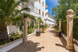 Un camino bordeado de macetas y palmeras que conduce a un edificio blanco con balcones y barandas de piedra.