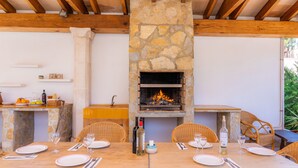 An outdoor dining area with stone walls, wooden beams, and wicker chairs. - Apartment Close to the Beach with Pool Access, Private Terrace, Air Conditioning and Wi-Fi (Canyamel)