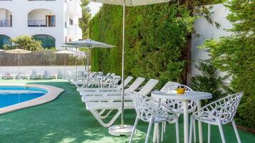 Un espace aménagé au bord de la piscine, avec des chaises longues et des tables, une piscine et un mur végétal.