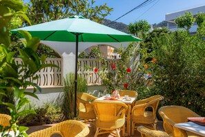 Un pati amb mobles de vimet, una taula posta amb plats i un parasol verd.