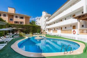 Una piscina amb gandules, una petita font i un edifici amb balcons.