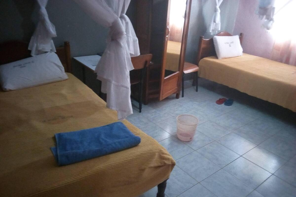 A dormitory room with two beds, a chair, and a small table.