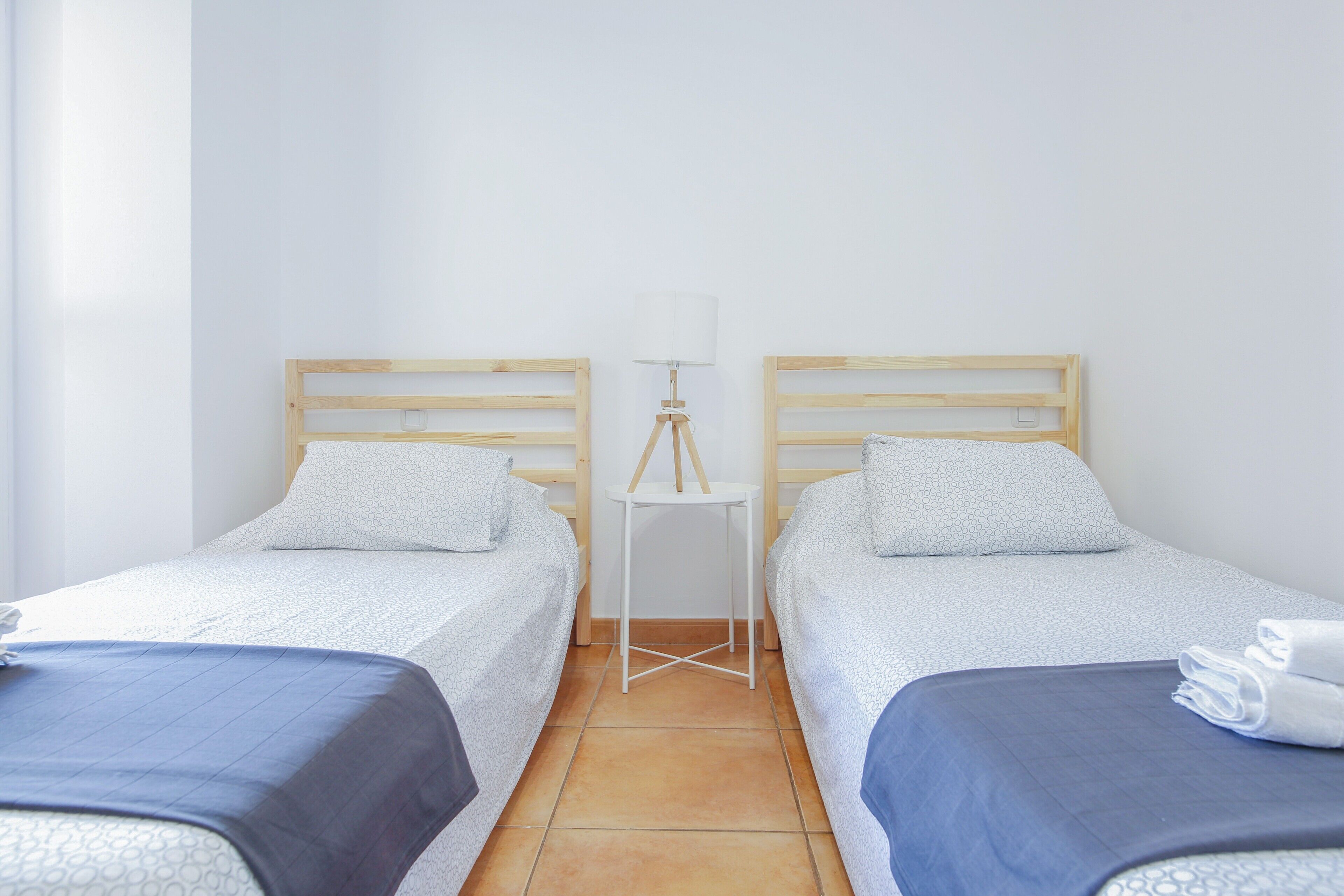 A hotel room with two single beds, a small table with a lamp, and a window.