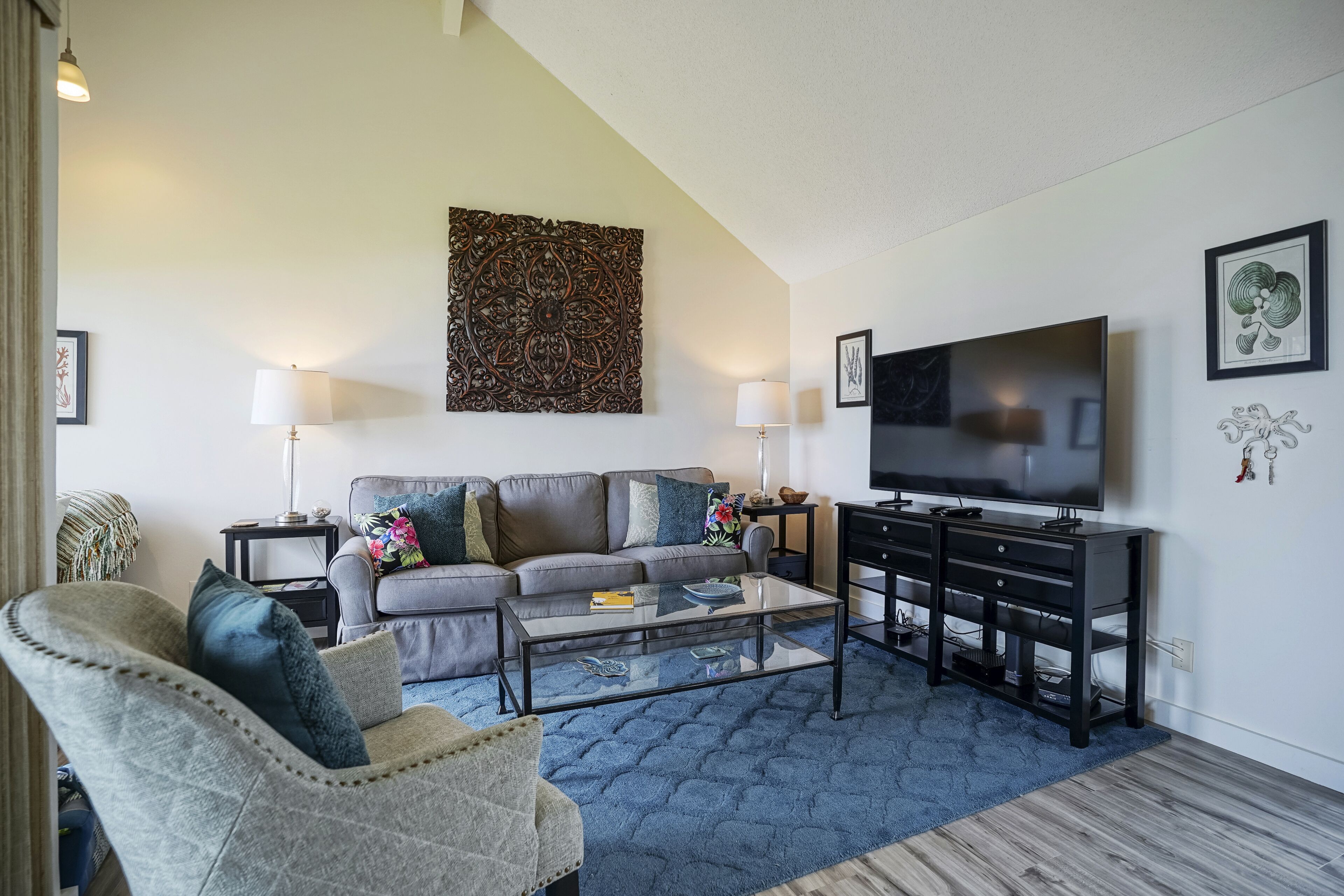 A living room with a sofa, armchair, coffee table, TV, and artwork on the walls.