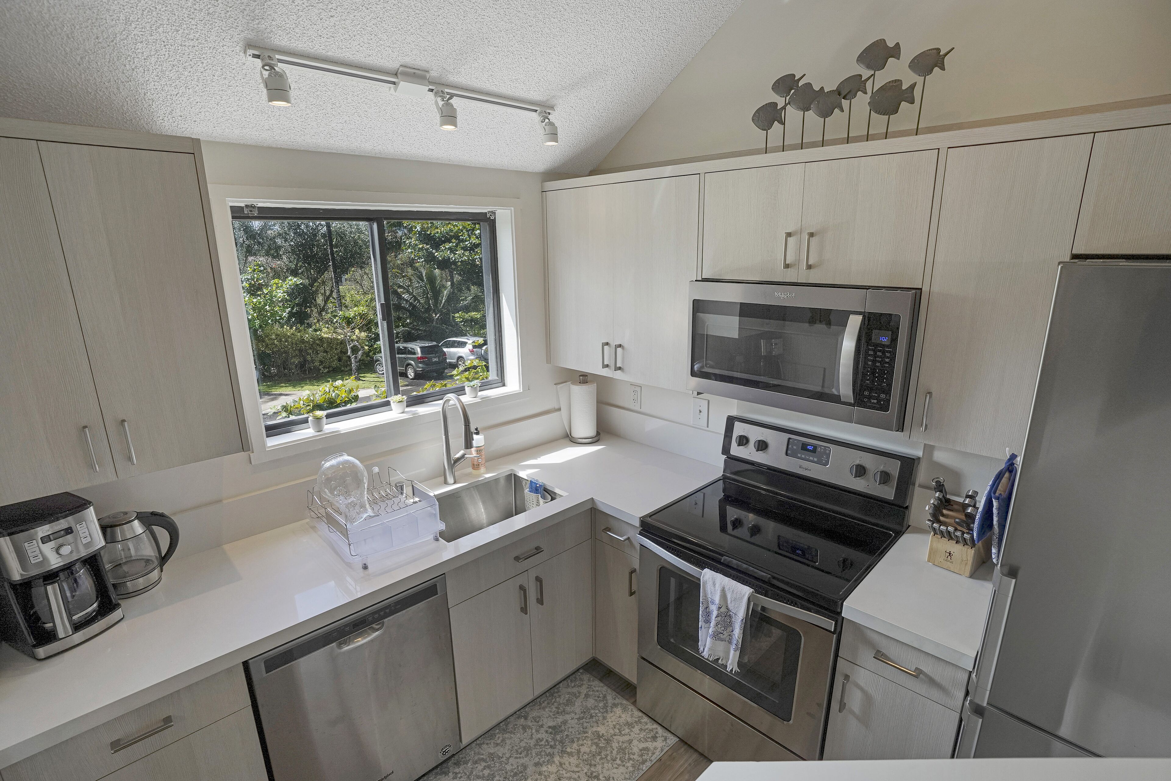 A modern kitchen with stainless steel appliances, a dishwasher, and a window providing a view of the outdoors.
