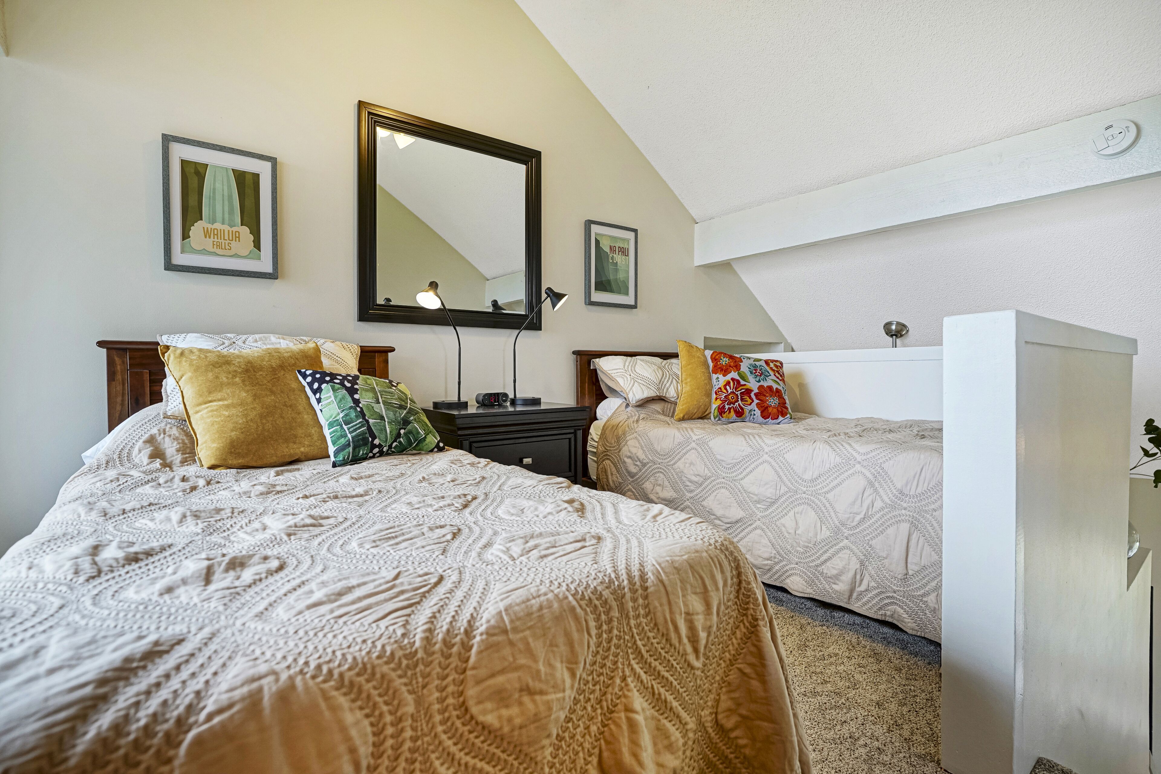 A bedroom with two beds, a large mirror, and framed pictures on the wall.