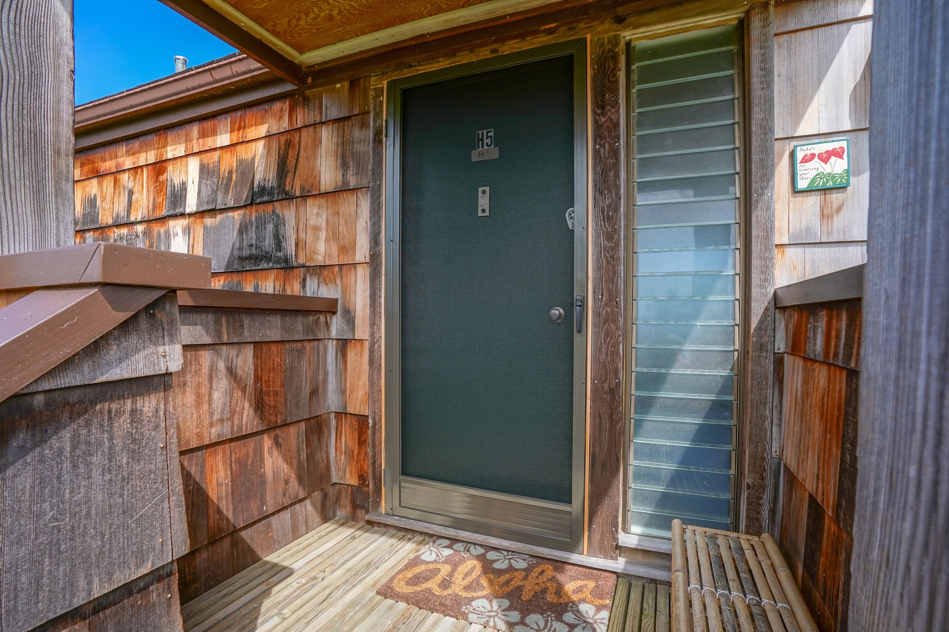 Une façade en bois avec une porte portant l’inscription « H5 » et un paillasson avec le mot « alpha ».