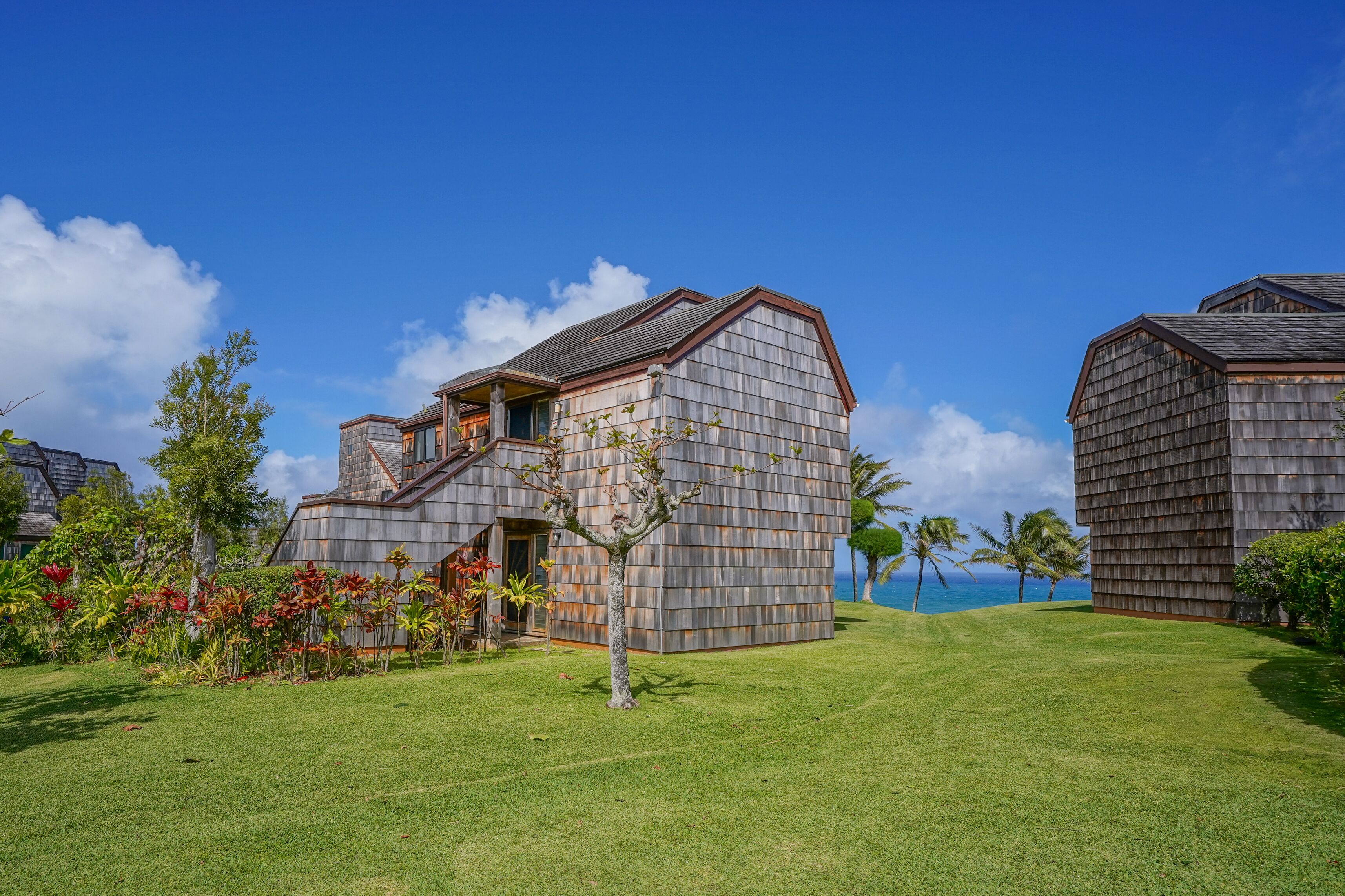 A modern building with a sloped roof, surrounded by a well-maintained lawn and tropical plants.