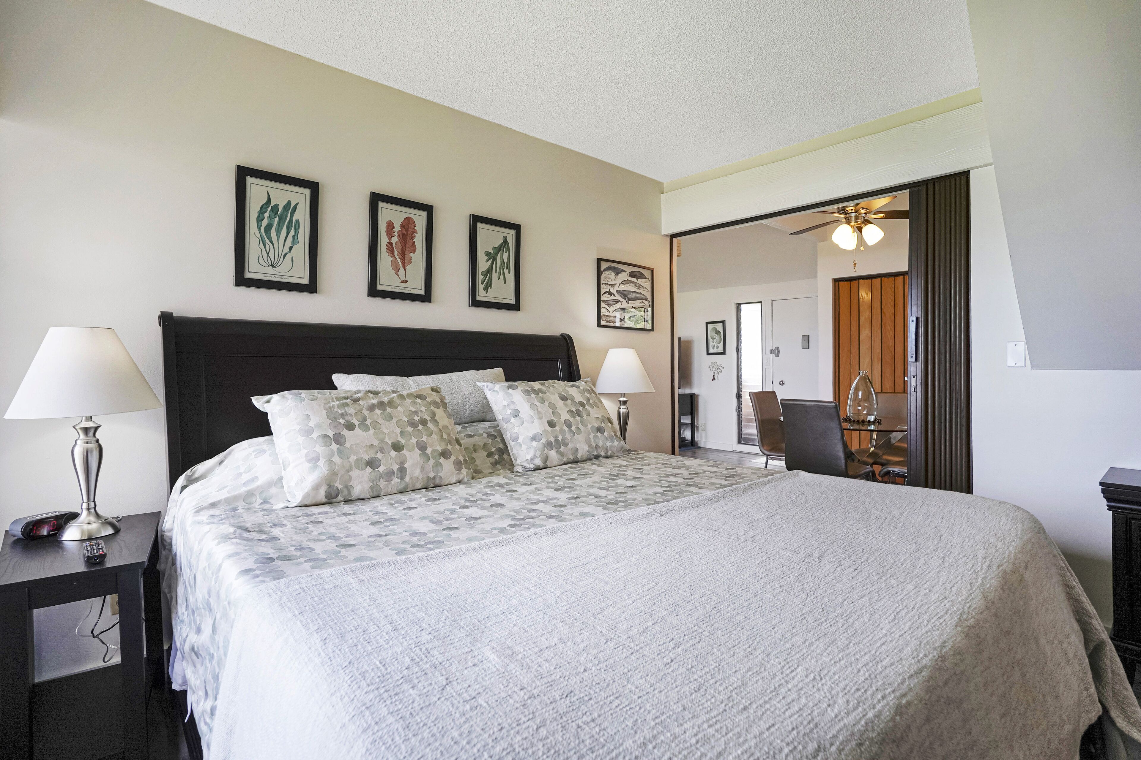 A neatly made bed with a grey and white patterned bedspread, two bedside lamps, and three framed botanical prints on the wall.