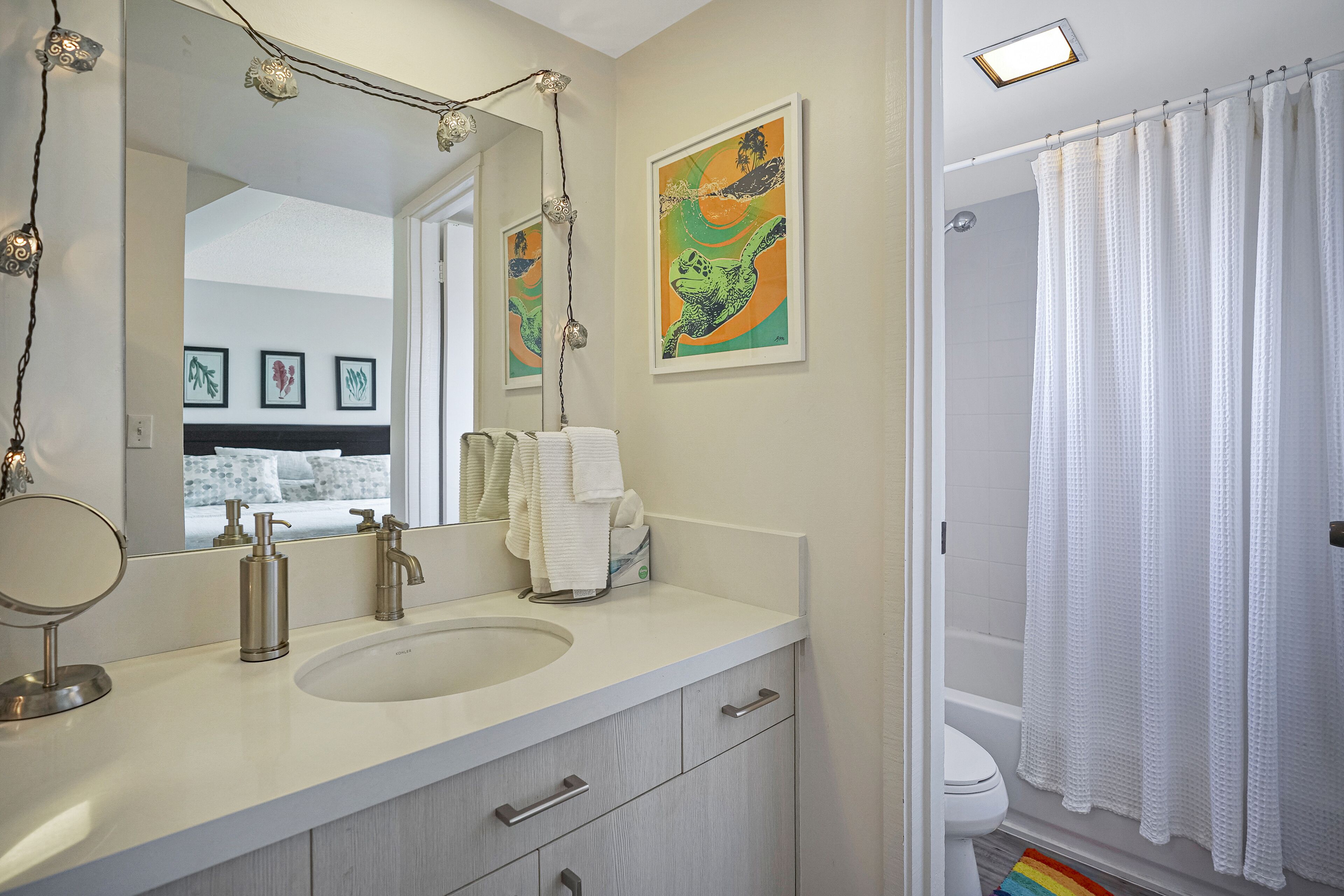 A bathroom with a sink, mirror, and towel rack. There are framed pictures on the wall and a shower curtain.