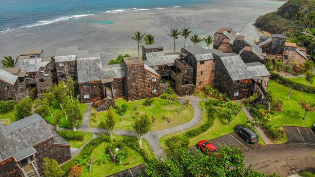 A coastal resort with wooden buildings, a parking area, and a view of the ocean. - Sealodge H5: Delightful Oceanview Condo, Close to Beaches & More (Princeville)