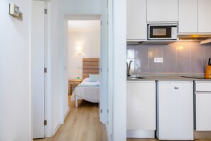 A compact hotel room with a bed, bedside table, and a kitchenette with a microwave and a small refrigerator. - Apartment Close to the Beach with Pool Access, Private Terrace, Air Conditioning and Wi-Fi (Canyamel)