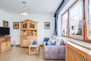 Un salon avec un meuble en bois, un canapé, une télévision et une fenêtre avec des rideaux.
