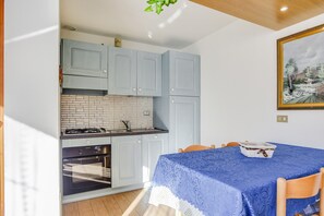 Une cuisine avec des meubles de couleur bleu clair, un plan de travail recouvert de carreaux blancs, une cuisinière et un four. On y trouve également une table à manger avec une nappe bleue et des chaises.